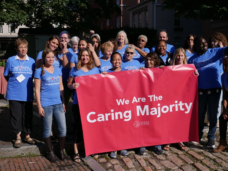A group of people wearing matching blue T-shirts hold a large banner that reads