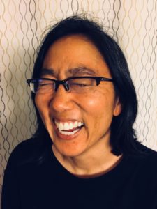 Stacy, a brown woman in glasses, is laughing and smiling really big.